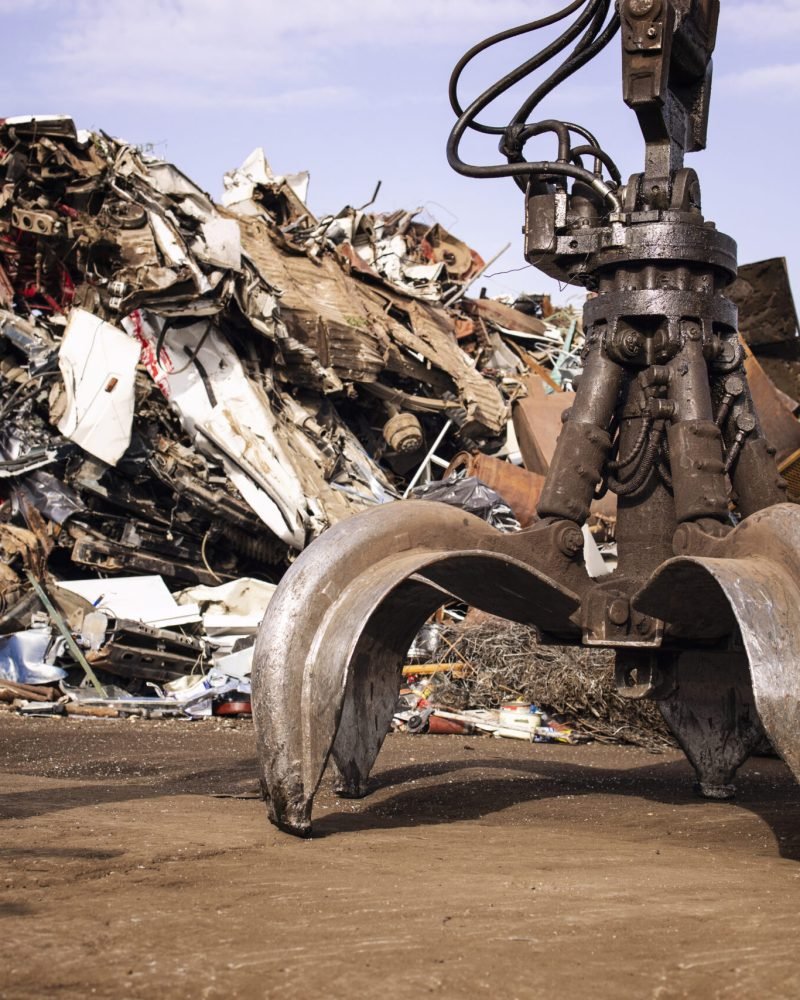 Metal junk yard with hydraulic lifting machine with claw attachment for scrap metal recycling.